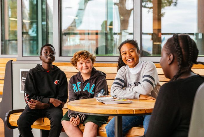 4 young people sitting on a bench smiling and listening to the young person in front of them