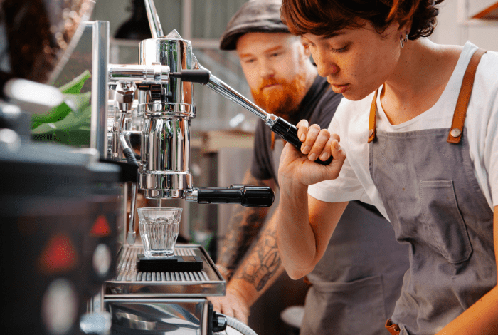 A young person and a trainer behind a coffee machine