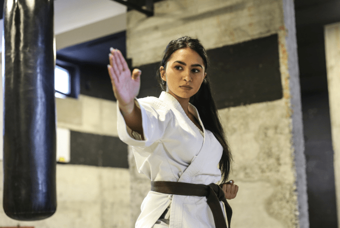 Woman in a white karate uniform with black belt hitting a punching bag 