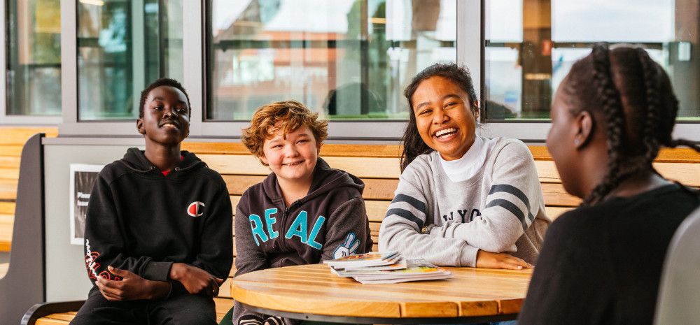 4 young people sitting on a bench smiling and listening to the young person in front of them
