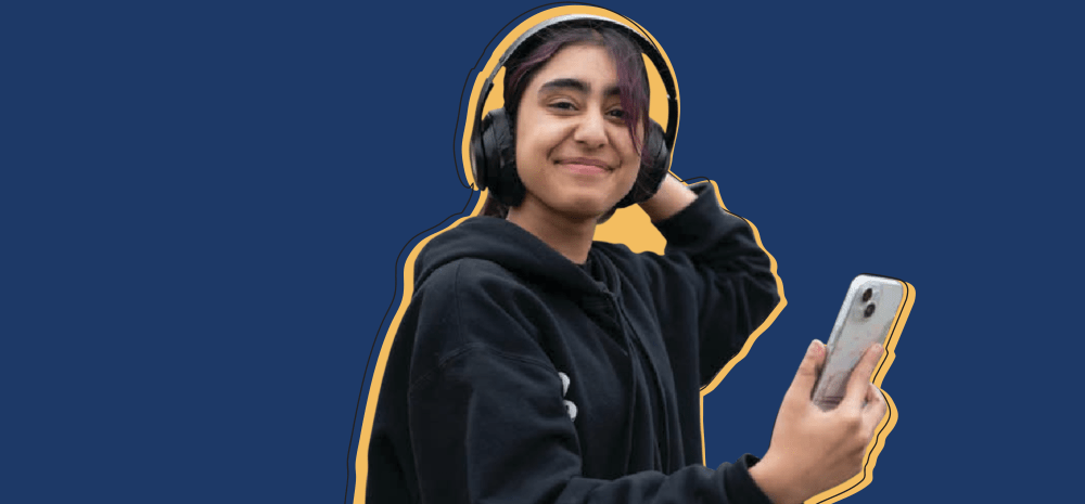 a young person holding a phone, wearing headphones, and smiling with a blue background