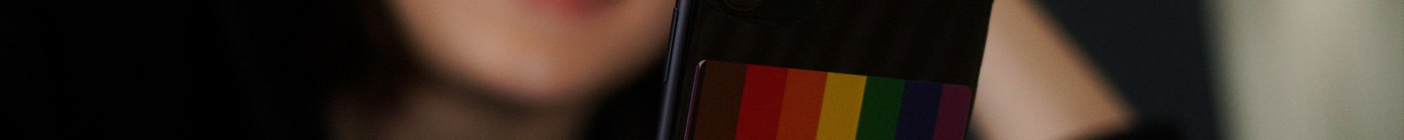 Young person lying on bed on the phone which has a rainbow flag sticker